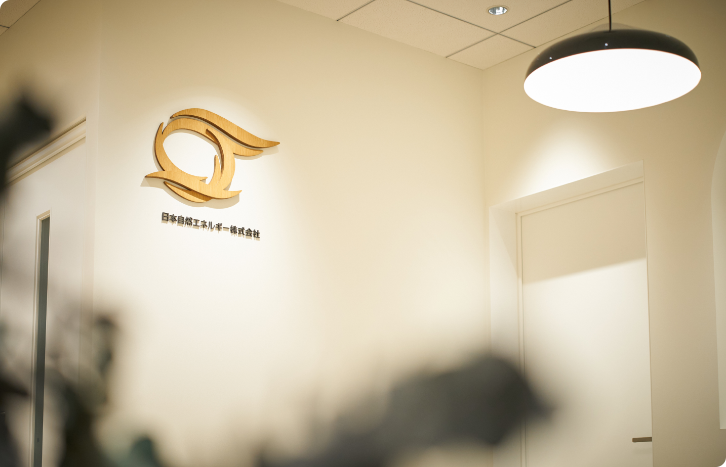 オフィスの壁に木製のロゴマークと「日本自然エネルギー株式会社」の社名が設置されている