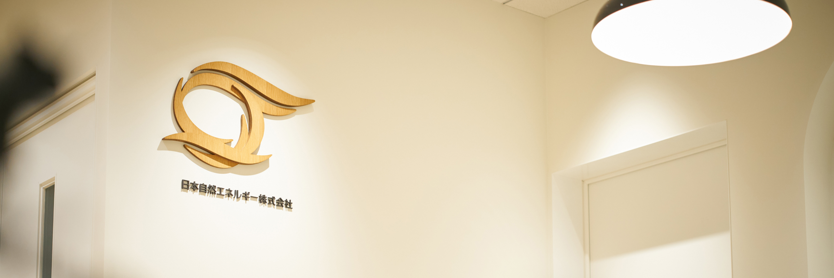 オフィスの壁に木製のロゴマークと「日本自然エネルギー株式会社」の社名が設置されている
