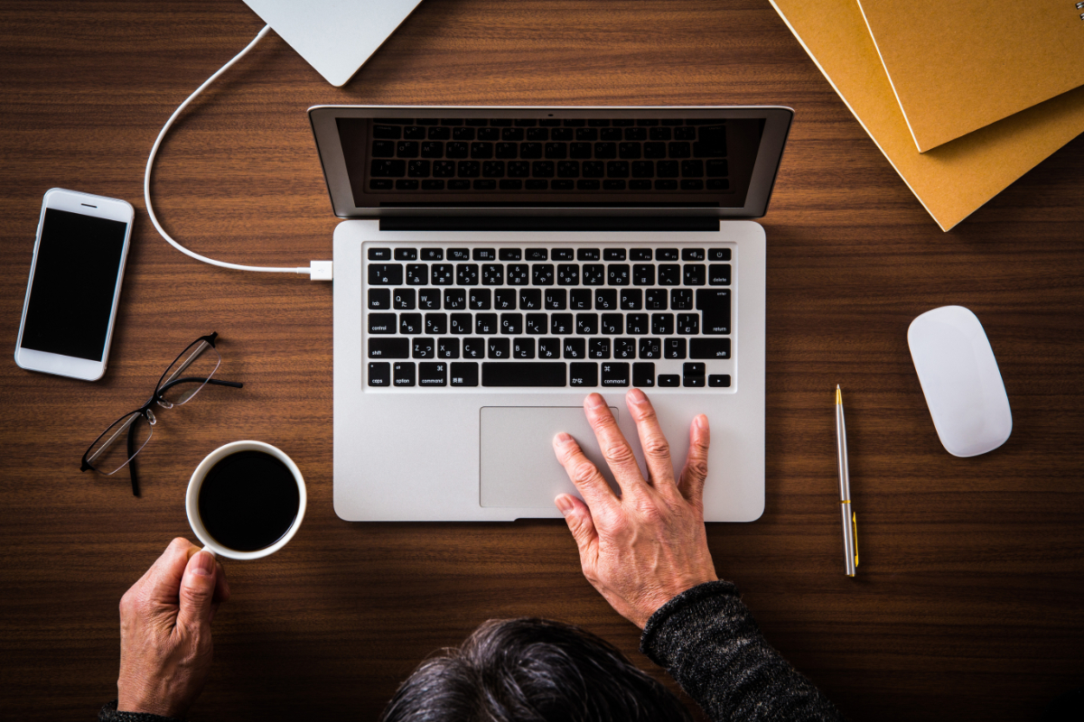 木製の机の上でノートパソコンを使って作業している人の上からの視点